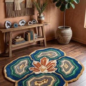 May include: A colorful, patterned rug with a gemstone design. The rug features shades of blue, green, gray, and gold, with a central crystal-like pattern. The rug is placed on a wooden floor, adding a decorative touch to the room.