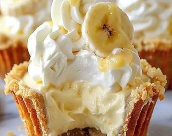 May include: Close-up of a mini banana cream pie with a golden-brown crust. The pie is filled with creamy custard, topped with whipped cream, and a banana slice. A drizzle of sauce adds a finishing touch. The pie has a bite taken out of it.