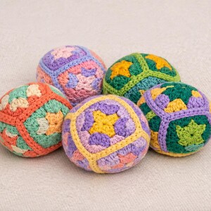 Puede incluir: Cinco bolas de ganchillo coloridas en tonos naranja, verde, morado y amarillo. Cada bola presenta un patr&oacute;n geom&eacute;trico &uacute;nico. Las bolas est&aacute;n dispuestas sobre una superficie neutra y texturizada.