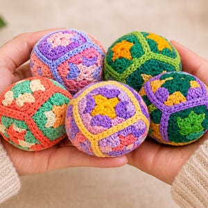 Puede incluir: Cinco bolas de ganchillo coloridas en tonos morado, verde, naranja y amarillo se sostienen en las manos de una persona. Las bolas tienen patrones geom&eacute;tricos y est&aacute;n hechas de hilo. El fondo es de color neutro.