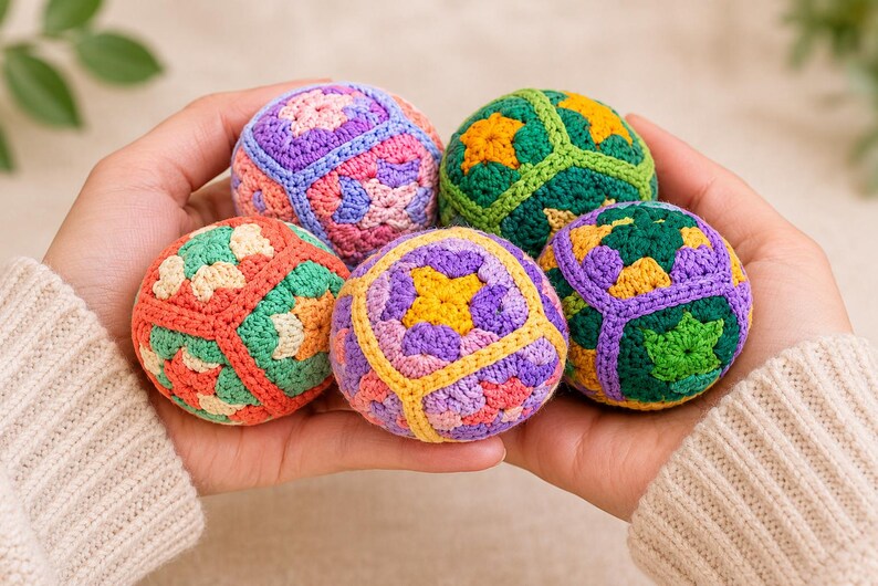 Puede incluir: Cinco bolas de ganchillo coloridas en tonos morado, verde, naranja y amarillo se sostienen en las manos de una persona. Las bolas tienen patrones geom&eacute;tricos y est&aacute;n hechas de hilo. El fondo es de color neutro.