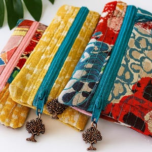 Könnte beinhalten: Nahaufnahme von vier farbenfrohen Reißverschlusstaschen mit Muster. Die Taschen weisen verschiedene Designs in Rosa-, Gelb-, Rot- und Blautönen auf. Jede Tasche hat einen türkisfarbenen Reißverschluss und einen dekorativen Baum-Anhänger.