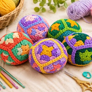 Puede incluir: Varias bolas de ganchillo de colores brillantes con patrones geom&eacute;tricos. Tambi&eacute;n se ven ganchos de ganchillo, hilo y peque&ntilde;as flores de ganchillo. La escena sugiere un proyecto de artesan&iacute;a con un enfoque en art&iacute;culos hechos a mano.