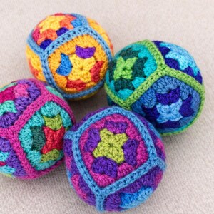 Puede incluir: Cuatro bolas de ganchillo coloridas en tonos morado, rosa, verde, azul, amarillo y naranja. Cada bola tiene un patr&oacute;n geom&eacute;trico y est&aacute; hecha con hilo. Las bolas est&aacute;n dispuestas sobre una superficie neutra y texturizada.