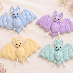 May include: Four plush bat ornaments in pastel colors: blue, purple, yellow, and teal. Each bat has white polka dots, stitched wings, and a smiling face. The bats are handmade and suitable for Halloween or nursery decor.