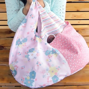 May include: A large, soft tote bag with a floral pattern in pink, blue, and yellow. The bag has a pink polka dot section and a striped section. The bag is held up by a person.