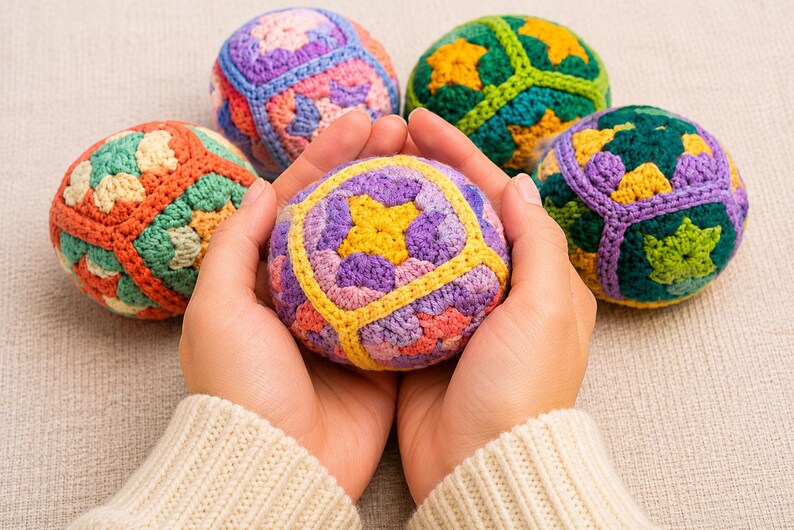 Puede incluir: Unas manos sostienen una colorida bola de ganchillo, rodeada de otras cuatro. Las bolas presentan patrones geom&eacute;tricos en tonos morado, amarillo, verde, naranja y azul. La persona lleva un su&eacute;ter color crema.