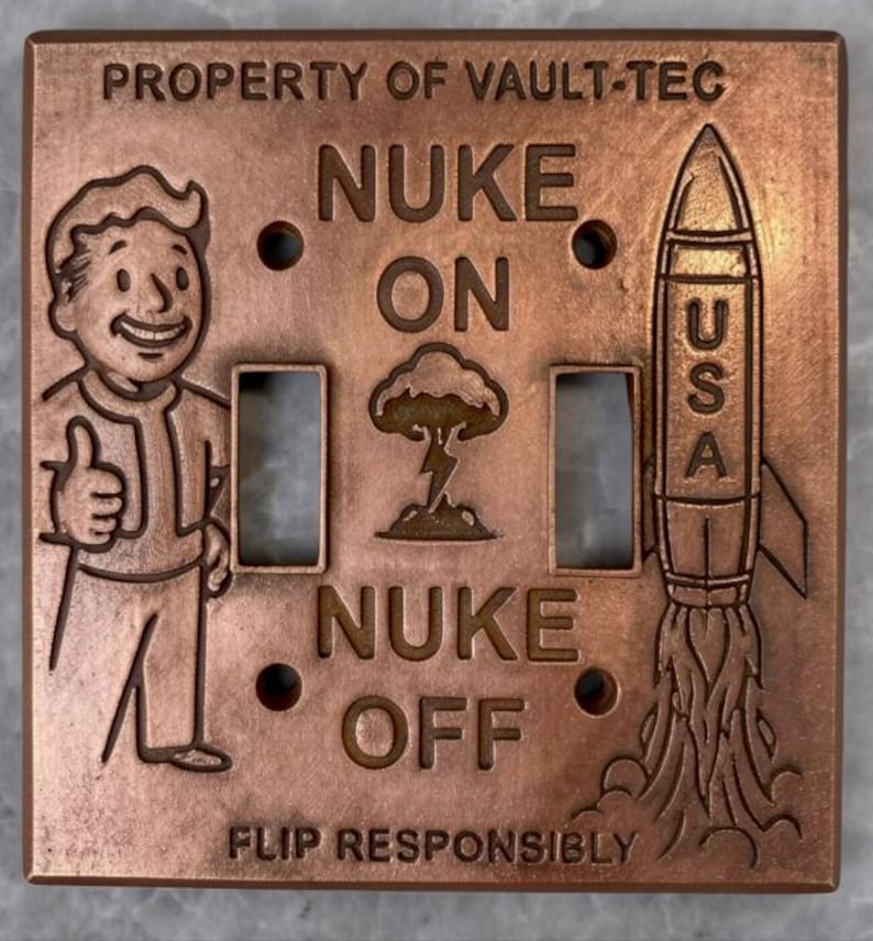 May include: A square copper-colored light switch plate featuring the text PROPERTY OF VAULT-TEC at the top and FLIP RESPONSIBLY at the bottom. It depicts a cartoon character giving a thumbs up, a mushroom cloud, and a rocket labeled USA.