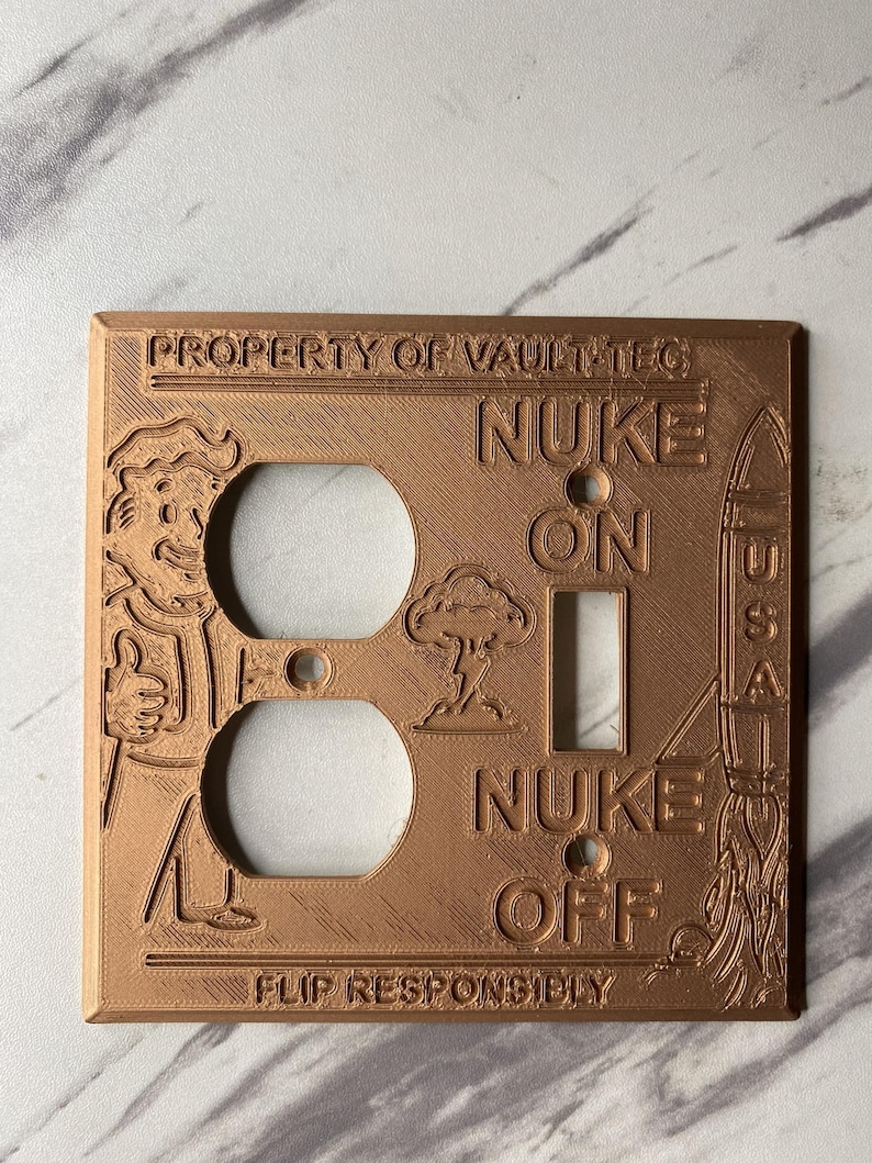 May include: A copper-colored rectangular light switch and outlet wall plate featuring embossed text that reads PROPERTY OF VAULT-TEC, NUKE ON, NUKE OFF, and FLIP RESPONSIBLY. The design includes a cartoon character, a mushroom cloud, and a rocket.