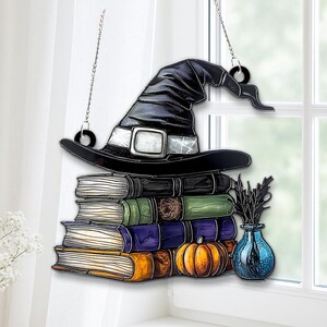 May include: A Halloween-themed hanging decoration featuring a black witch hat atop a stack of books. A small orange pumpkin and a blue vase with black stems are also included in the design. The decoration hangs from a chain.