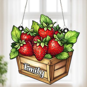 May include: A wooden sign featuring a watercolor illustration of ripe strawberries and green leaves overflowing from a wooden crate. The name "Emily" is written on the crate. The sign hangs from a chain.