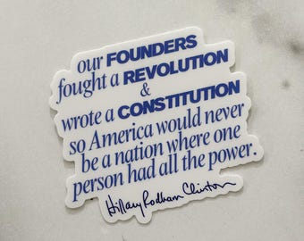 May include: A white sticker with blue text. The text reads: "Our Founders fought a Revolution & wrote a Constitution so America would never be a nation where one person had all the power." Signed "Hillary Rodham Clinton."
