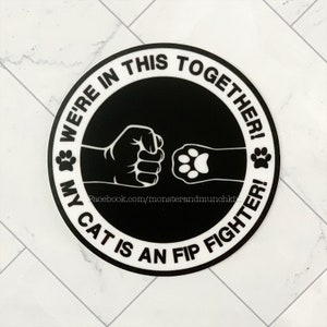 May include: Black and white round sticker with the text "We're in this together! My cat is an FIP fighter!" and a fist bumping a paw print.