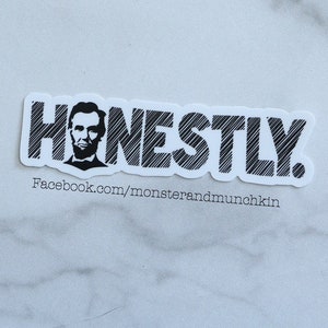 May include: Black and white sticker with the word "HONESTLY" in a stylized font. The word is outlined in black and has a textured, hatched pattern. A black and white image of Abraham Lincoln is incorporated into the "H" of the word. The sticker also includes the text "Facebook.com/monsterandmunchkin".