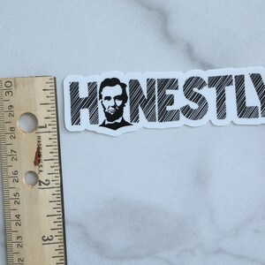 May include: A white sticker with black text that reads "HONESTLY."  A black and white image of Abraham Lincoln is in the "H".