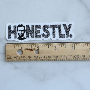 May include: A white sticker with black text that reads "HONESTLY."  The text is in a stylized font with a black and white image of Abraham Lincoln's face in the "H".
