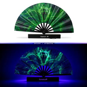 May include: A folding hand fan with black ribs and a green graphic print of a snake with an open mouth. The base is black with the white text funxtuff. The fan is shown in daylight and under UV light, where the green snake design glows brightly.