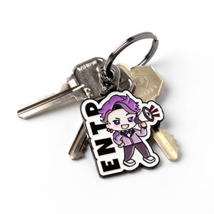 May include: A metal keychain featuring a cartoon character with purple hair holding a megaphone, next to the bold black text ENTP. The charm is attached to a dark metal split ring that holds two silver-colored metal keys with visible teeth.
