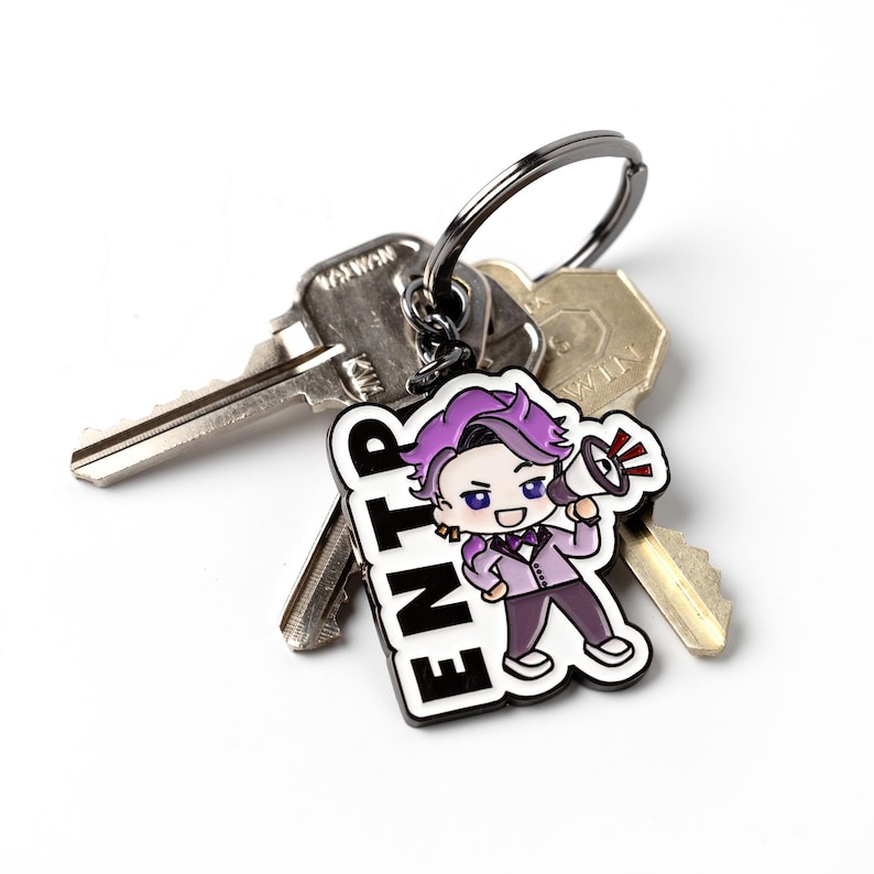 May include: A metal keychain featuring a cartoon character with purple hair holding a megaphone, next to the bold black text ENTP. The charm is attached to a dark metal split ring that holds two silver-colored metal keys with visible teeth.