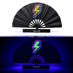 May include: A black folding hand fan featuring a pixelated yellow and blue lightning bolt graphic. The base of the fan is marked with the text fun: tuff. The fan is shown in two states: daylight and UV reactive, where the bolt glows green.