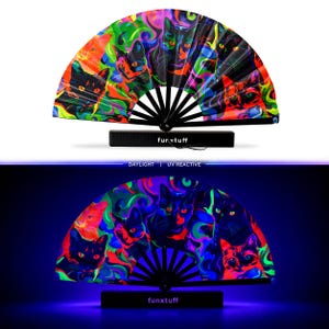 May include: A folding hand fan with a black frame and a vibrant, psychedelic cat print featuring neon colors that glow under UV light. The fan displays multiple cat faces amidst swirling patterns and includes the text funxtuff on the handle.