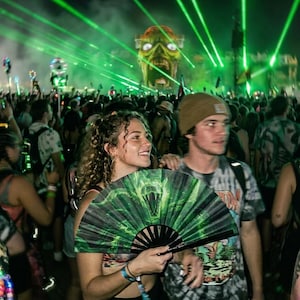 May include: A handheld folding fan featuring a green and black graphic print of a snake with bared fangs. The fan is held open, displaying the detailed illustration against a dark background with bright green laser lights and a large monster head.