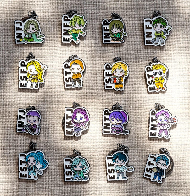 May include: A collection of sixteen enamel keychains, each featuring a cartoon character and a four-letter personality type acronym including INFJ, ENFP, INFP, ENFJ, ESFP, ISTP, ISFP, ESTP, INTJ, ENTJ, INTP, ENTP, ESTJ, ISFJ, ESFJ, and ISTJ.