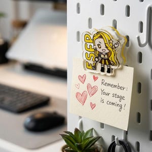May include: A clear acrylic magnet featuring a cartoon character with long blonde hair, a brown skirt, and a microphone, with the yellow text ESFP. The magnet holds a cream-colored note with red hand-drawn hearts and the text Remember: Your stage is coming!