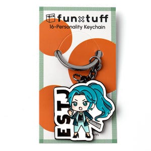 May include: An enamel keychain on a display card labeled funxtuff 16-Personality Keychain. The keychain features a cartoon character with teal hair, a dark blazer, and light pants, holding a ruler. The text ESTJ is printed in large black letters.