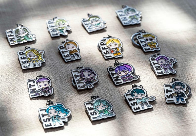 May include: A collection of sixteen metal enamel keychains, each featuring a unique anime-style character illustration paired with a four-letter personality type acronym such as INFJ, ENFP, ISTP, ISFP, ESTP, ESFP, ENTJ, INTP, ENTP, INTJ, ESFJ, and ISTJ.
