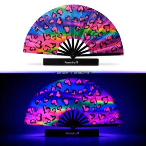 May include: A folding hand fan with a rainbow gradient background and black heart outlines. The fan features black ribs and a black base with the text funxtuff printed in white. The bottom section shows the fan glowing under UV light.