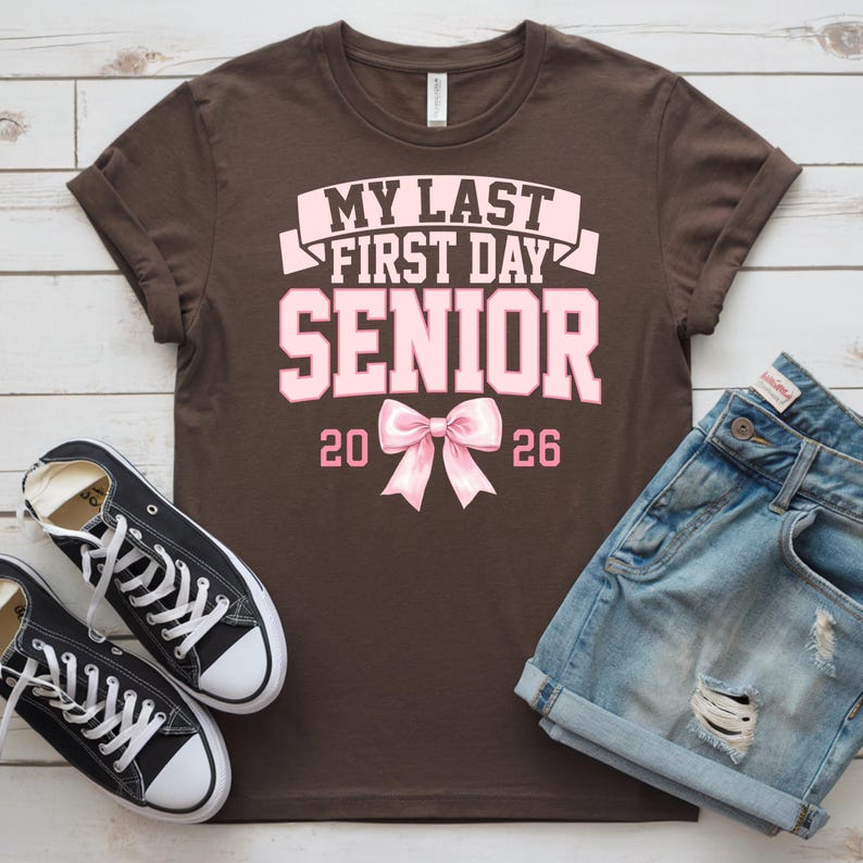 May include: A brown t-shirt with the text "MY LAST FIRST DAY SENIOR 2026" in pink. The shirt is paired with denim shorts and black canvas sneakers with white laces.
