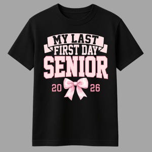 May include: Black t-shirt with the text "MY LAST FIRST DAY SENIOR 2026" in pink and white. A pink bow graphic is centered below the word "SENIOR". The shirt is a crew neck style.