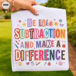 May include: A white t-shirt featuring the colourful text "BE LIKE SUBTRACTION AND MAKE A DIFFERENCE" in a playful, blocky font. The design is decorated with small graphic elements including stars, smiley faces, crayons, bows, and red apples.