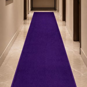 May include: A long, rectangular, deep purple hallway runner rug. The rug is centered in a hallway with light-colored walls, doors, and a marble floor. The runner adds a pop of color to the neutral space.