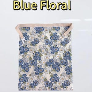 Peut inclure: Un sac en tissu rectangulaire avec un motif floral bleu sur fond blanc. Le sac comprend une sangle beige avec une boucle &agrave; d&eacute;gagement lat&eacute;ral en plastique blanc sur le dessus. Le texte "Blue Floral" est imprim&eacute; en jaune au-dessus du sac.