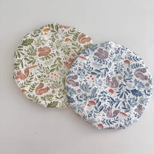 Peut inclure: Deux articles de tissu ronds et décorés. L'un présente un fond blanc avec des écureuils bruns, des feuilles vertes et des champignons orange. L'autre a un fond blanc avec des écureuils violets, des feuilles bleues et des champignons rouges.