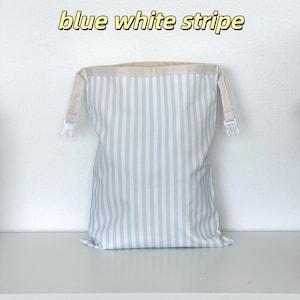 May include: A rectangular fabric bag featuring a vertical blue and white stripe pattern. The top edge is finished with a beige fabric trim and includes two white plastic side-release buckles. The text "blue white stripe" appears above the bag.