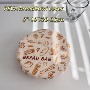 Peut inclure: Une housse de bol &agrave; pain ronde en PEVA avec un bord &eacute;lastique, en tissu cr&egrave;me imprim&eacute; d'illustrations marron de divers pains, p&acirc;tisseries et &eacute;pis de bl&eacute;, avec le texte BREAD BAG. Elle convient aux r&eacute;cipients de 20 &agrave; 25 cm.