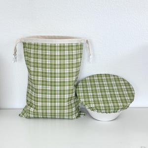 May include: A green and white plaid drawstring bag and bowl cover set. The bag is tall and cylindrical with a beige rim and drawstring closure. The bowl cover is round and elasticized. Both items are made of fabric.