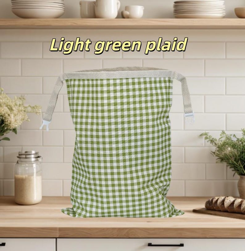 Peut inclure: Un sac en tissu rectangulaire avec un motif &agrave; carreaux vert clair et blanc. Le sac pr&eacute;sente une large ouverture sup&eacute;rieure de couleur claire avec deux sangles lat&eacute;rales et des clips en plastique blanc. Le texte "Light green plaid" est inscrit au-dessus.