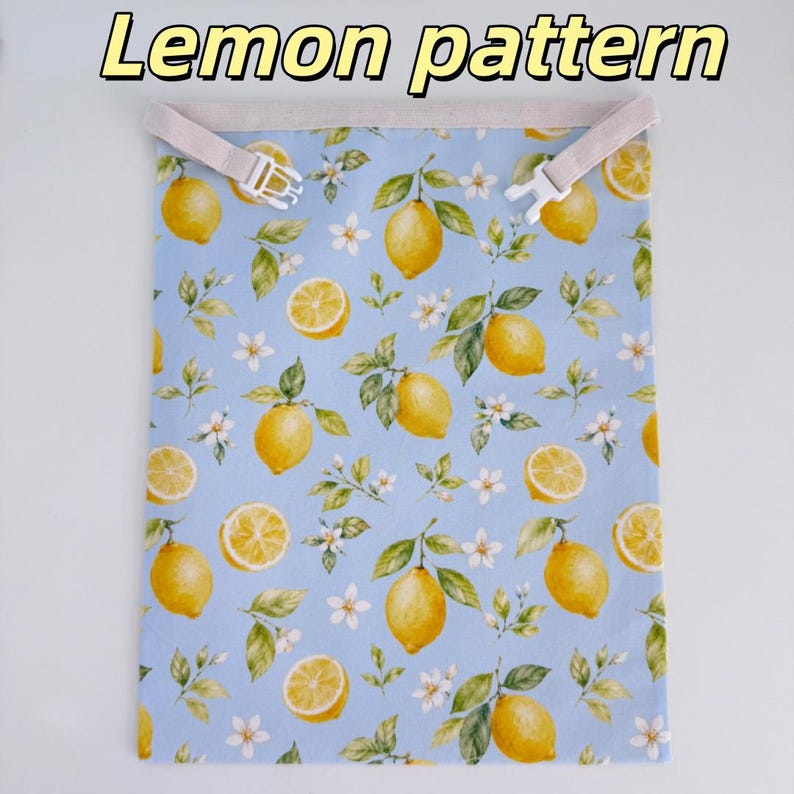Peut inclure: Un sac en tissu rectangulaire avec un fond bleu clair orn&eacute; d'un motif r&eacute;p&eacute;titif de citrons jaunes, de feuilles vertes et de fleurs blanches. Le bord sup&eacute;rieur comporte une sangle beige avec une boucle en plastique blanc. Texte Lemon pattern.