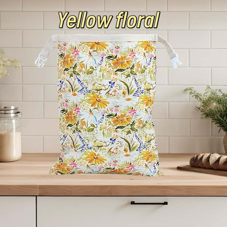 Peut inclure: Un sac &agrave; cordon rectangulaire pr&eacute;sentant un fond blanc avec un motif vibrant de tournesols jaunes, de petites fleurs roses et de fleurs sauvages bleues. Le texte "Yellow floral" est imprim&eacute; en jaune au-dessus du sac, dot&eacute; de sangles blanches.