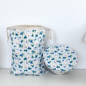 May include: A fabric storage bag and bowl cover set. The items feature a blue and white striped pattern with illustrations of blueberries and white geese. The bag has a drawstring closure and the bowl cover is round.