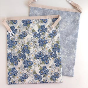 Peut inclure: Deux sacs en tissu avec des sangles beiges et des boucles en plastique. Un sac présente un fond blanc avec des motifs floraux bleus et blancs. L'autre sac a un motif bleu clair moucheté. Les deux sacs sont ouverts en haut.