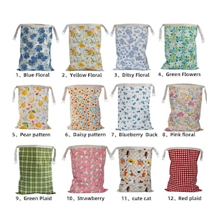 Op de afbeelding: Collectie van twaalf trekkoordtassen met diverse patronen. Ontwerpen omvatten blauwe bloemen, gele bloemen, groene bloemen, perenpatroon, madeliefjespatroon, roze bloemen, groene ruit, aardbeien, schattige kat en rode ruit.