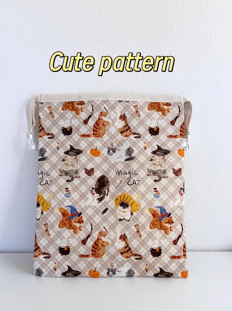 Peut inclure: Un sac &agrave; cordon rectangulaire avec un fond &agrave; carreaux beige et un motif r&eacute;p&eacute;titif de chats portant des chapeaux de sorci&egrave;re, des citrouilles, des chaudrons et des baguettes. Le texte "Cute pattern" est en haut et "Magic CAT" est imprim&eacute;.