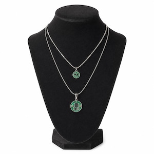 May include: Two silver necklaces with circular green circuit board pendants on a black display. The necklaces have different lengths, with one pendant smaller than the other. The pendants have a silver border.