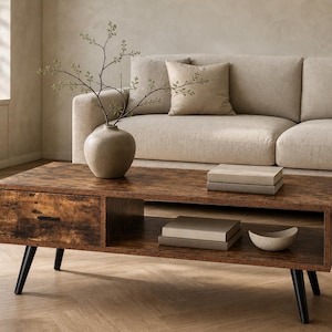 May include: A rustic brown coffee table with a drawer and open shelf, supported by black legs. The table holds books, a decorative bowl, and a vase with greenery. A beige sofa and pillows are in the background.