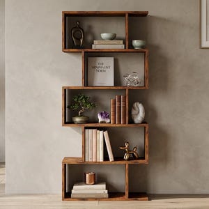 May include: A modern, wooden bookshelf with a unique, zig-zag design. The shelves display books, decorative objects, and a small bonsai tree. The text on the book reads "THE MINIMALIST FORM". A potted olive tree stands to the left.